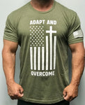 Olive green short sleeve t-shirt. Fabric is 60% Combed Ring-Spun Cotton, 40% Polyester Crew neck. Front of t-shirt has a large logo in white print. Message is "adapt and overcome" and has a picture of an altered American flag turned on it's side with a cross formed on one of the white stripes. Left sleeve has a small American flag screen printed in white on the bottom of the sleeve