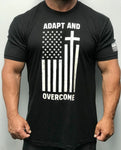 Black short sleeve t-shirt. Fabric is 60% Combed Ring-Spun Cotton, 40% Polyester Crew neck. Front of t-shirt has a large logo in white print. Message is "adapt and overcome" and has a picture of an altered American flag turned on it's side with a cross formed on one of the white stripes. Left sleeve has a small American flag screen printed in white on the bottom of the sleeve.