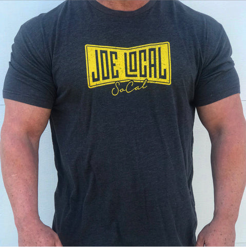 Front of the t-shirt. Dark grey t-shirt with yellow Joe Local So Cal flag logo at the center of the chest. Well fitted and comfortable t-shirt. Fabric: CVC Jersey 60% Combed Ring-Spun Cotton 40% Polyester /32 singles, 145 grams/4.3 oz  Neck: Crew